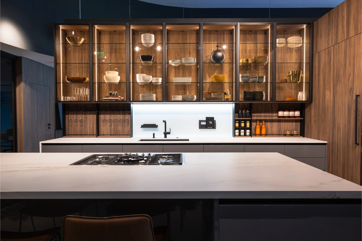 Luxury Italian kitchen display at Rastelli's Los Angeles showroom featuring glass-front upper cabinets, a marble island with integrated gas cooktop, and warm accent lighting.