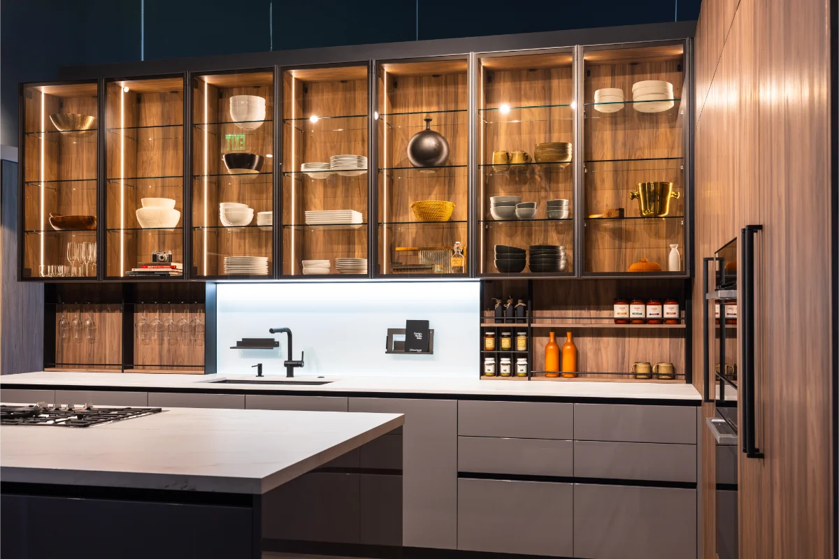 Italian kitchen with illuminated glass-front upper cabinets displaying dishware, matte grey lower drawers, white marble countertop, black matte faucet, and open shelving with integrated storage at Rastelli's Los Angeles showroom