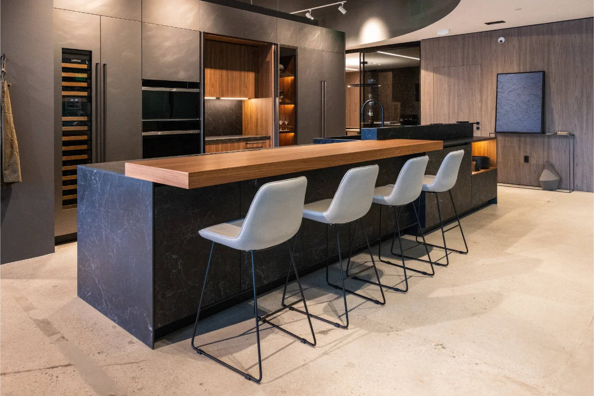 Luxury Italian kitchen display at Rastelli's Los Angeles showroom featuring a dark stone island with walnut top, four bar stools, integrated wine fridge, and wall ovens in a complete showroom environment